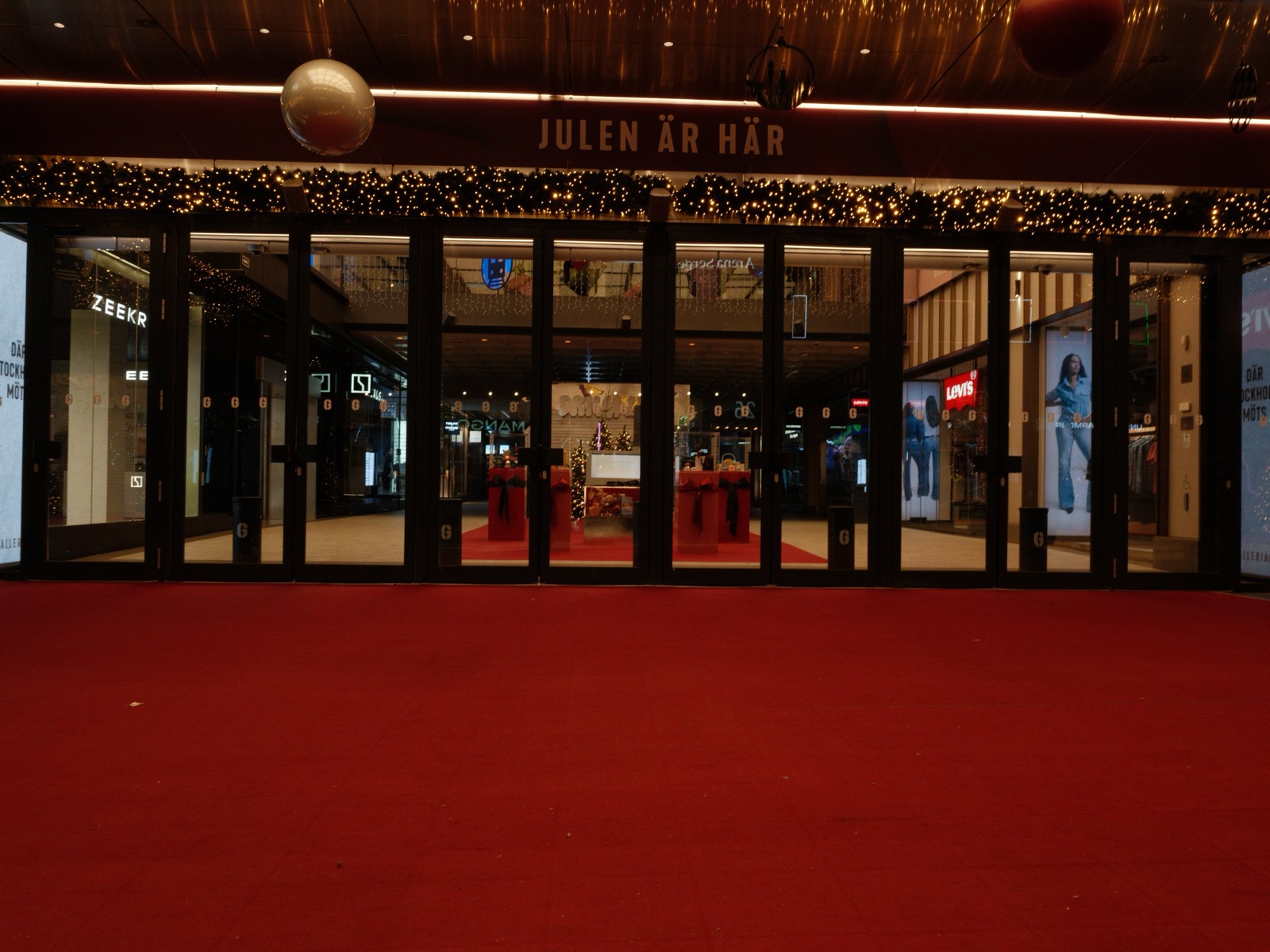 Red carpet laid over level ground at a mall entrance with wide doors and Christmas decorations