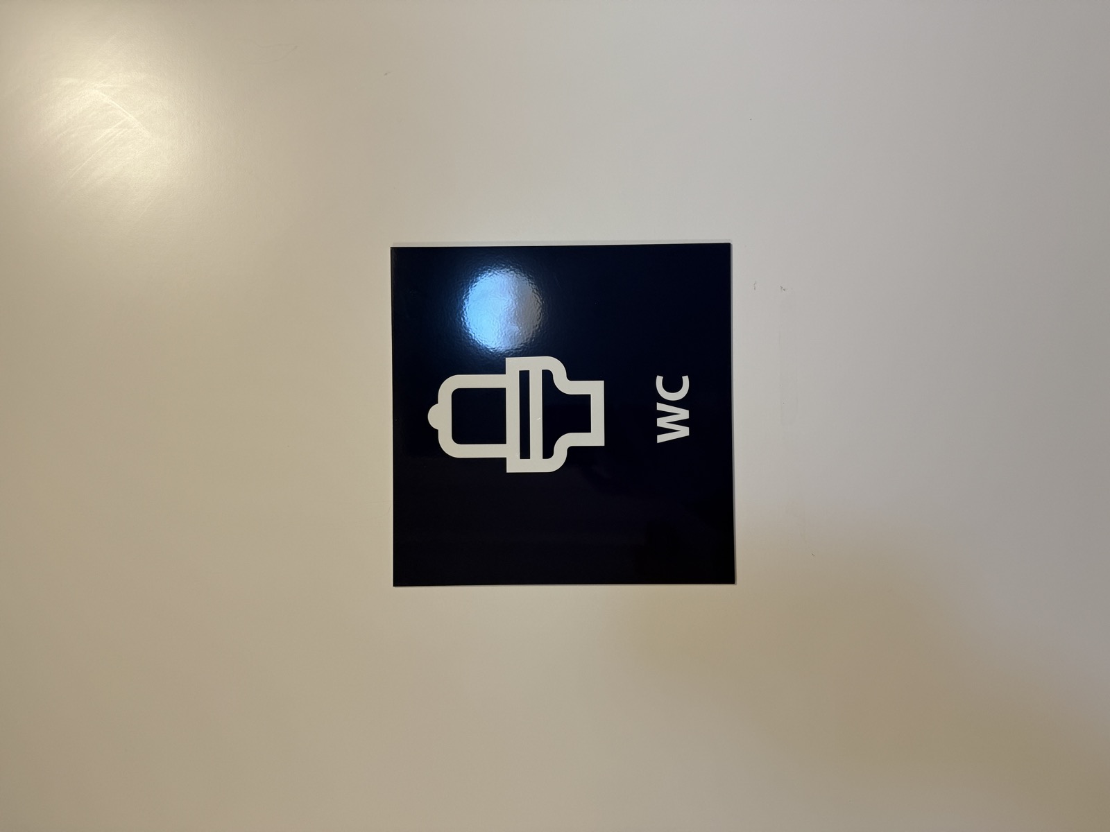 Dark blue square sign with a white toilet pictogram and the letters WC set vertically beside it.