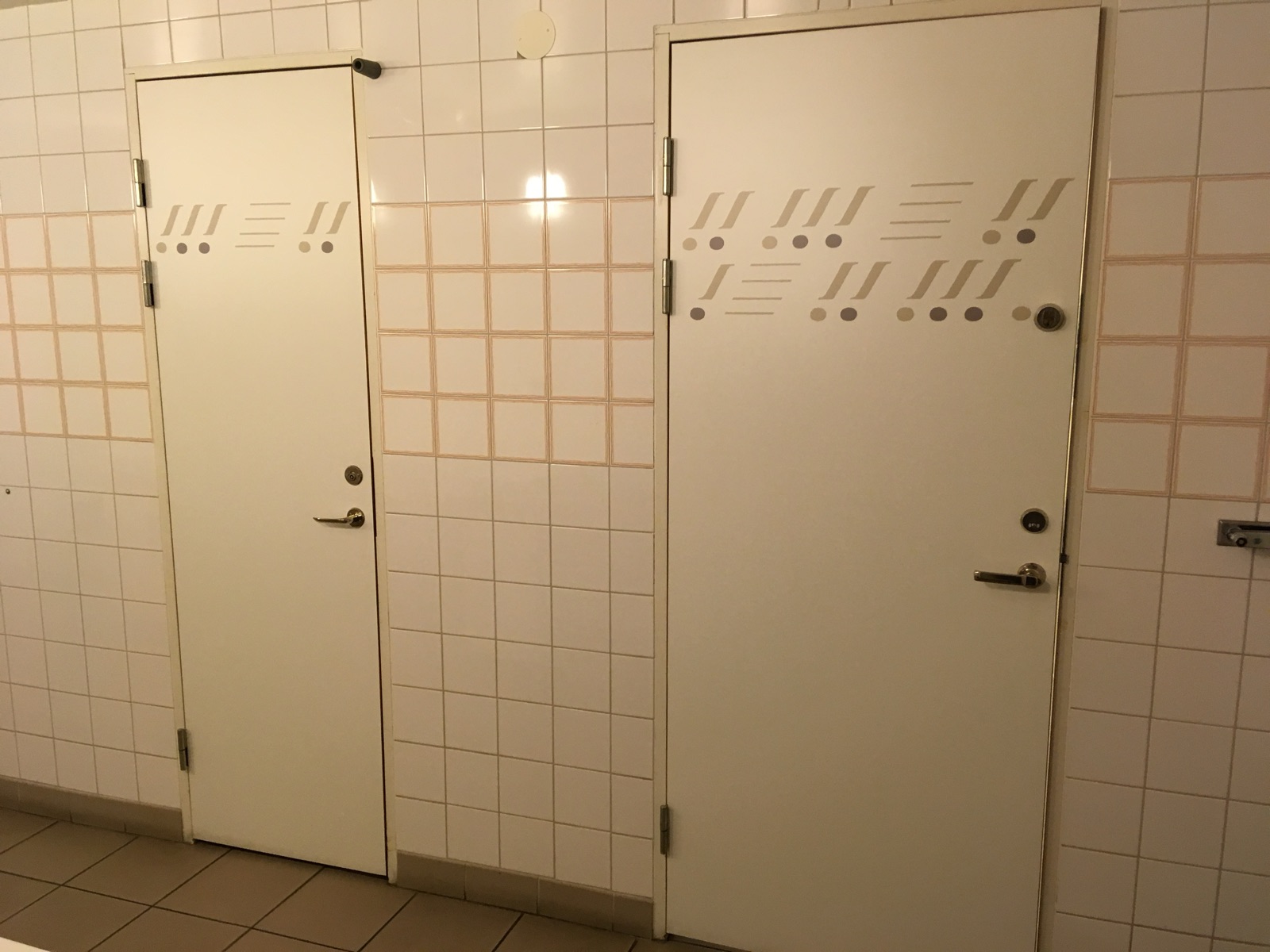 Two toilet cubicle doors of clearly different widths, each decorated with a band of lines and dots