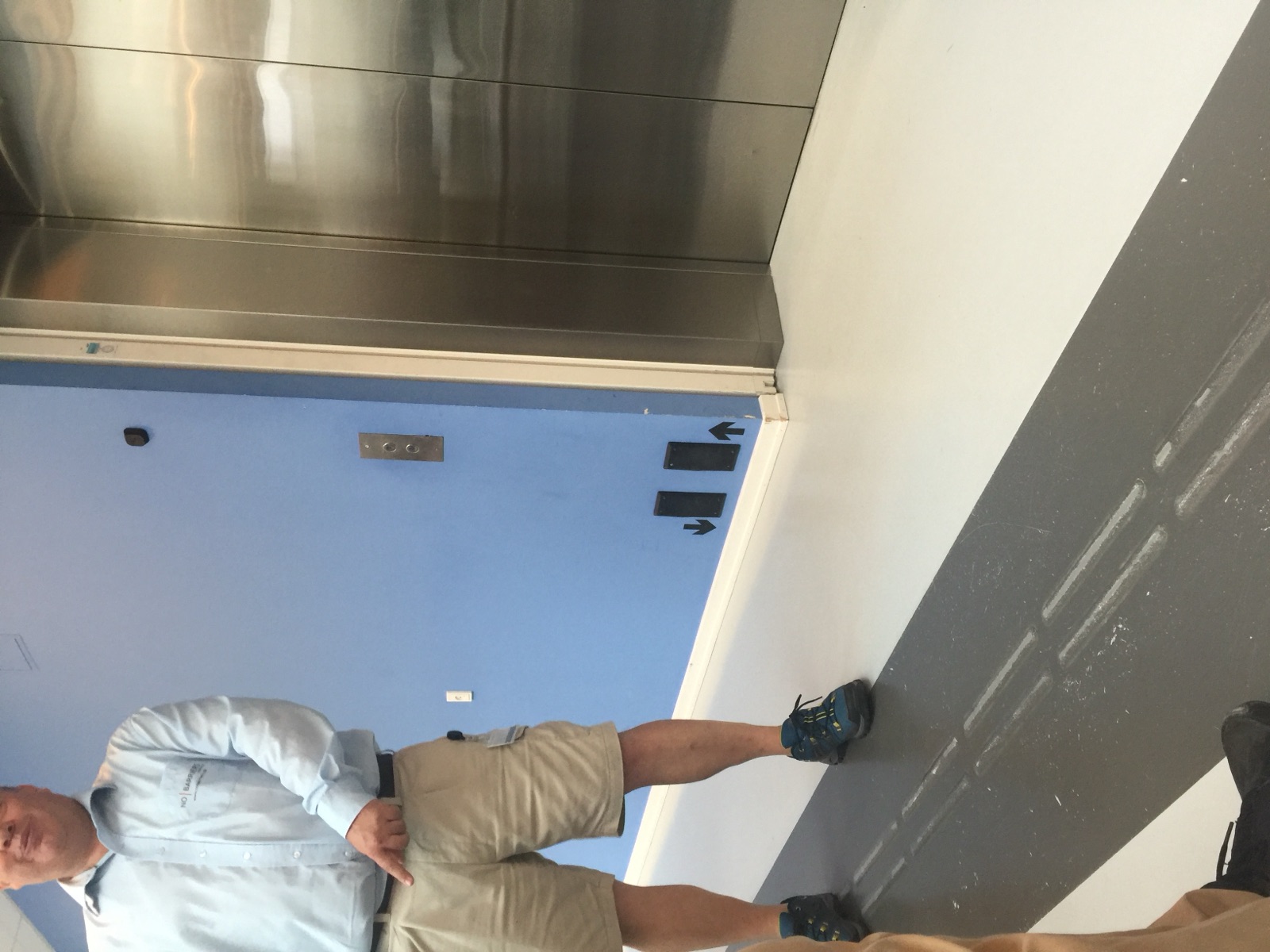 Elevator call buttons repeated at foot height beside the door, with a shoe pressing one