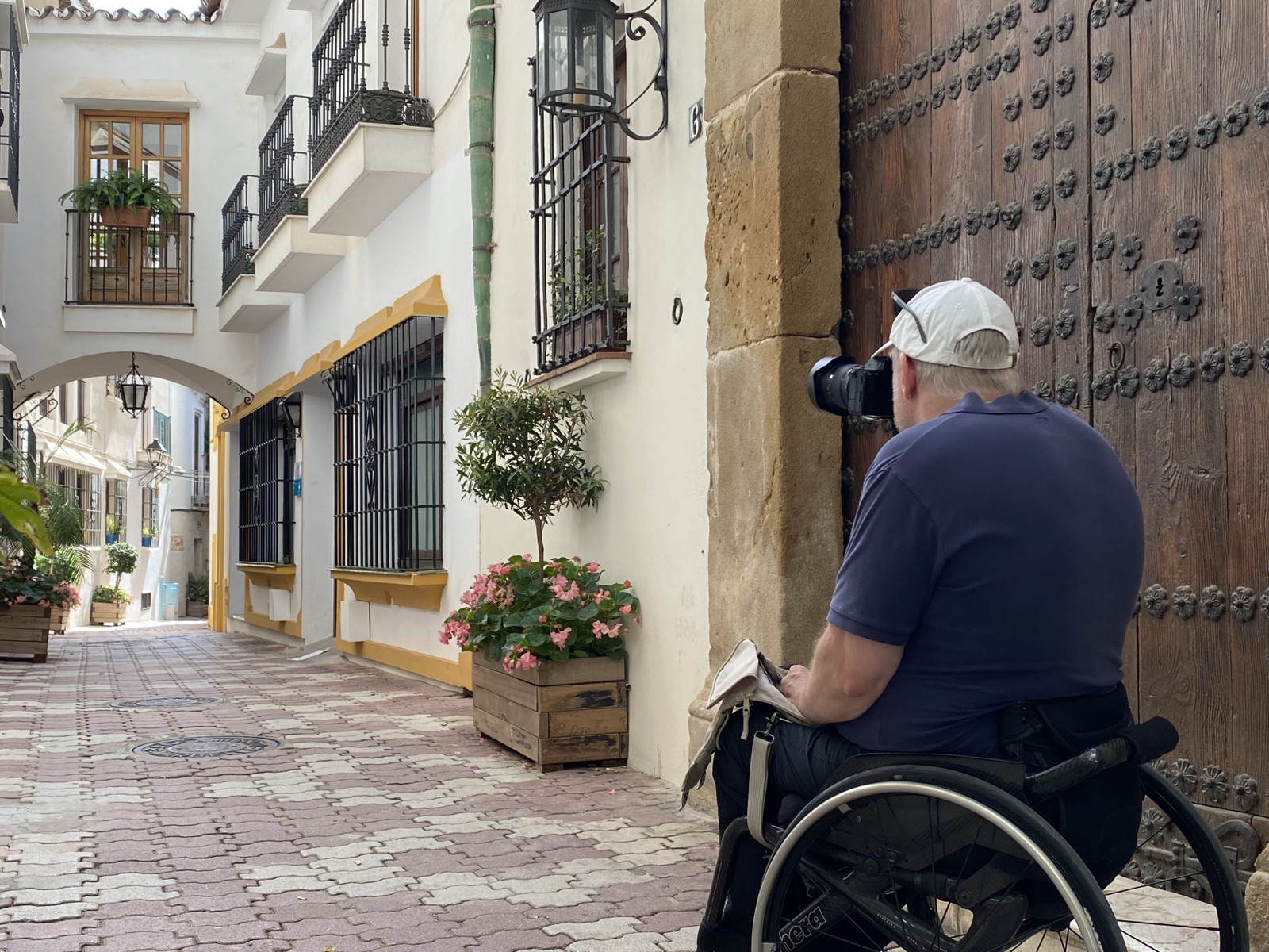 Per-Olof from behind in his wheelchair, camera raised, photographing a studded wooden door in a narrow whitewashed street