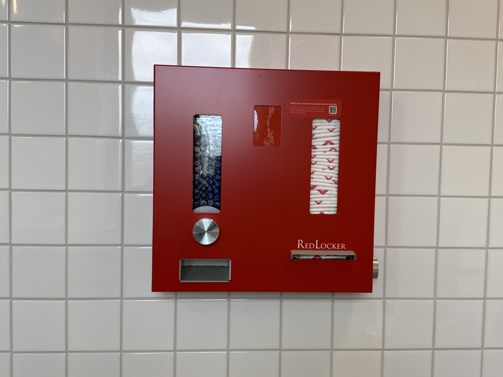 Bright red dispenser for tampons and pads mounted on a restroom wall