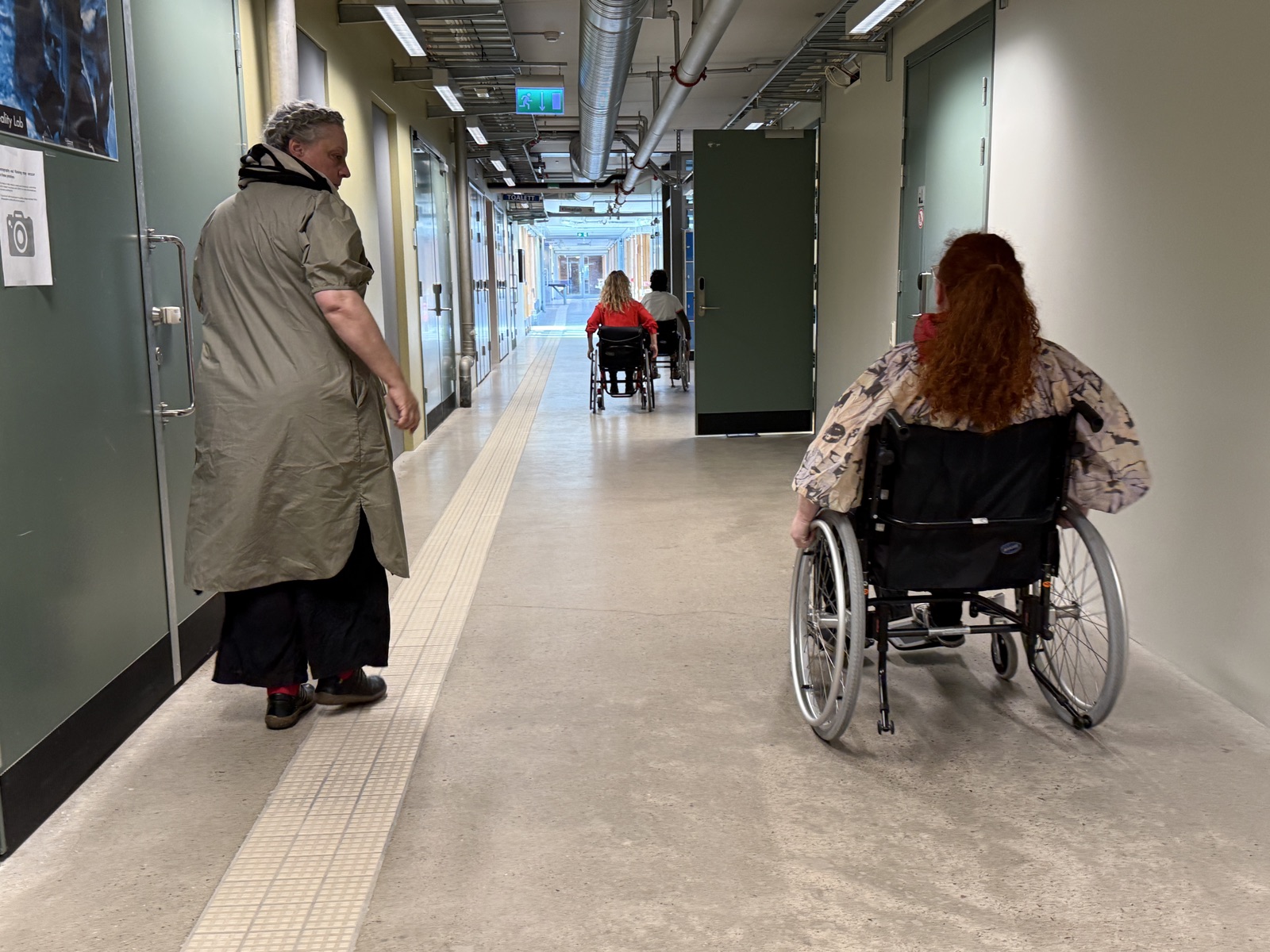 Wide university corridor with several people, walking and in wheelchairs, moving side by side