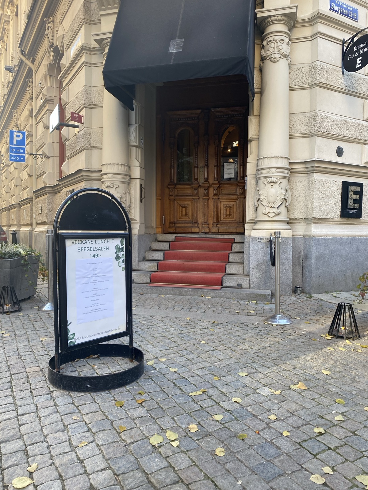 The entrance of a historic hotel in Sundsvall. An ornate stone portal with columns frames carved oak double doors, and a red runner covers the granite steps up to them.