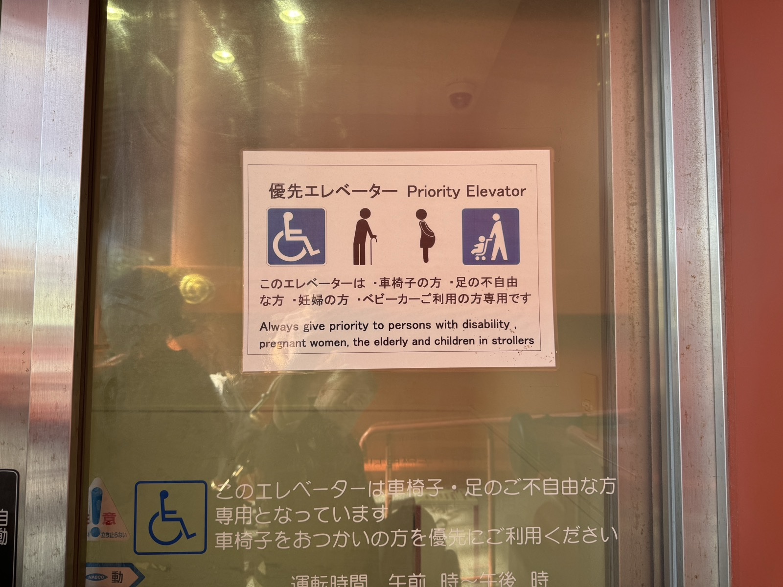 Priority Elevator notice on a glass elevator door at the Sensō-ji temple in Tokyo, with four icons, a wheelchair user, an older person with a cane, a pregnant person, and a parent pushing a stroller.