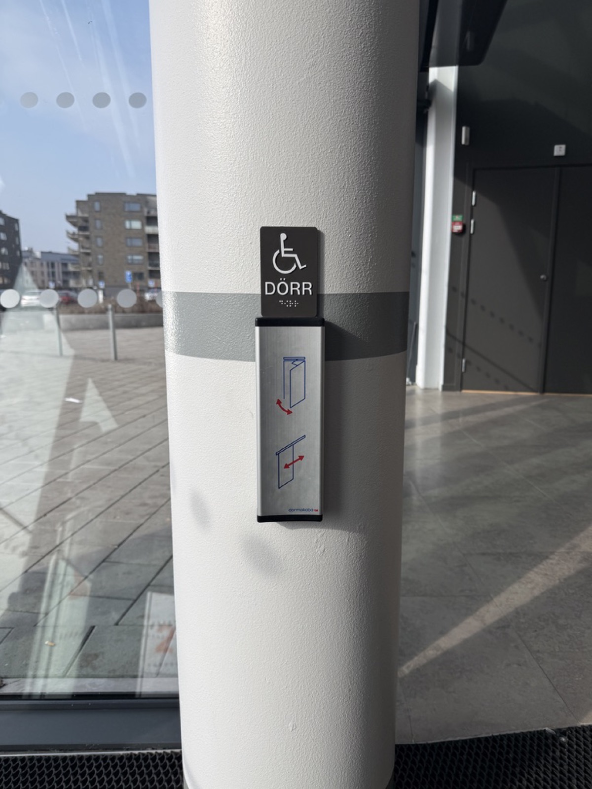 Automatic door button on a pillar in Sweden, a wheelchair symbol with the word DOOR in Swedish above it and pictograms showing the door mechanism.