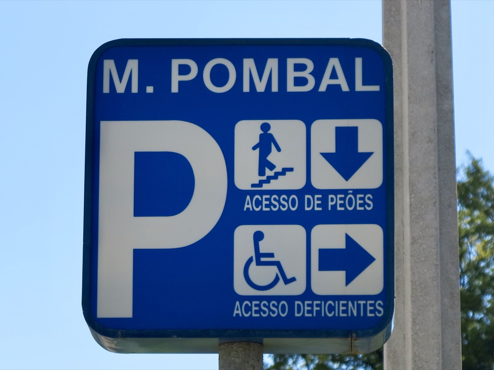 Blue parking sign in Portugal with a two-route system: Acesso de peões, pedestrian access, with a person on stairs and a down arrow; Acesso deficientes with a wheelchair symbol and an arrow pointing another way.