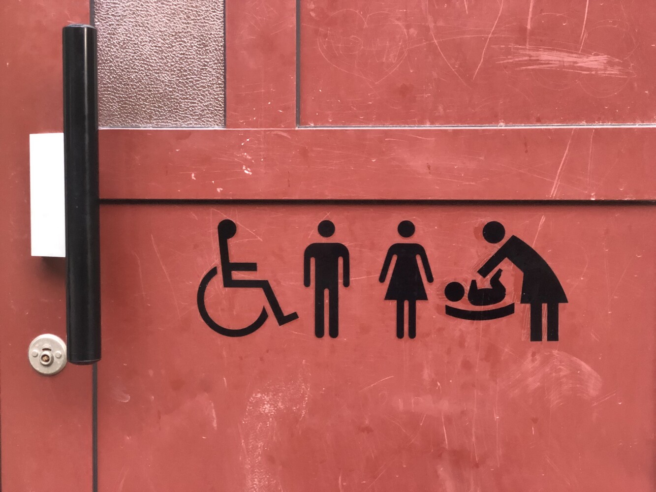A toilet door with symbols for wheelchair user, man, woman, baby changing.