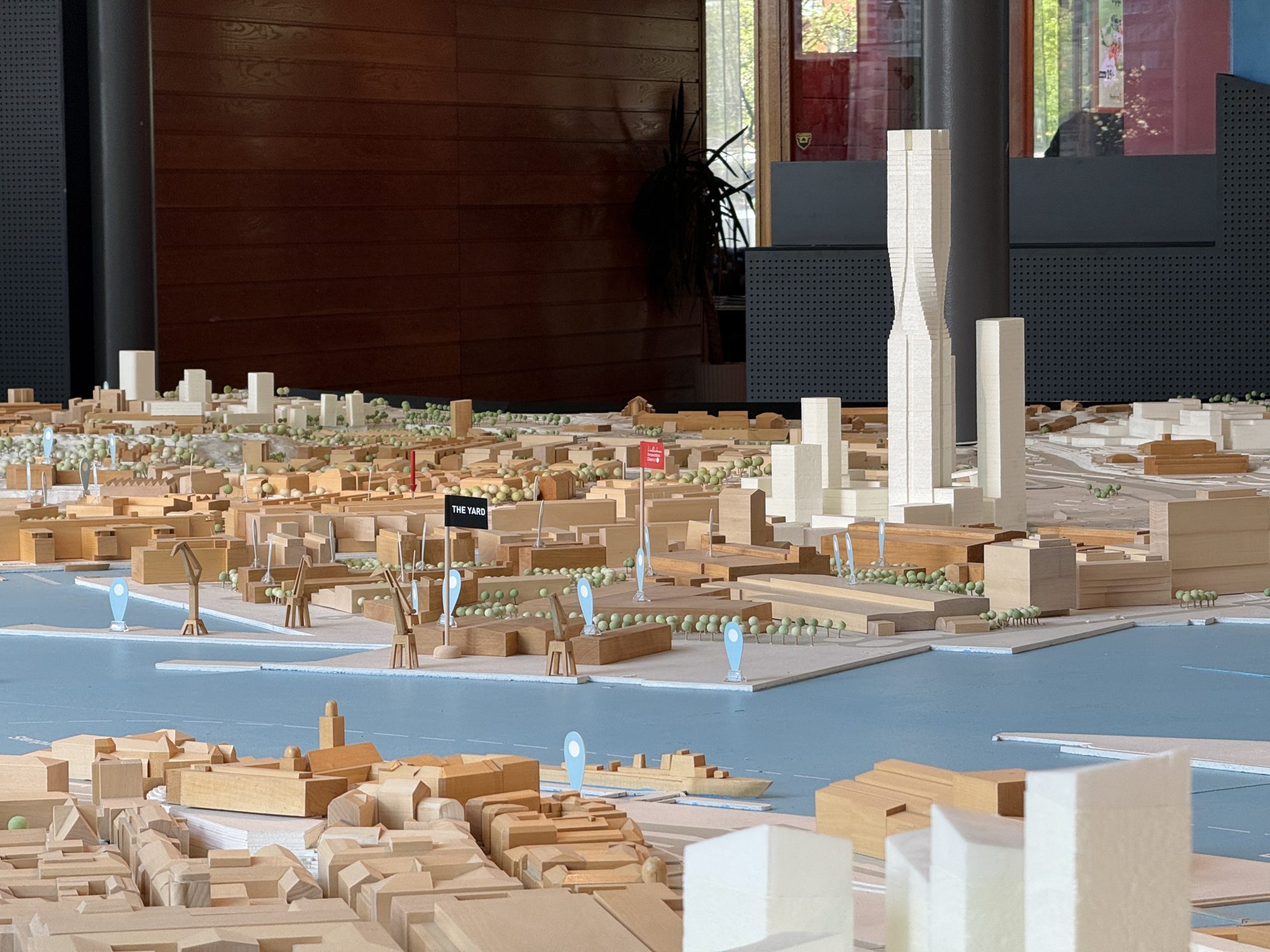 Älvstadsmodellen i Göteborg i skala 1:400. Den befintliga staden i trä, de planerade husen i vitt, älven i ljusblått med hamnkranar, och små flaggor som markerar The Yard och Lindholmen Innovation District. Karlatornet reser sig i mitten.