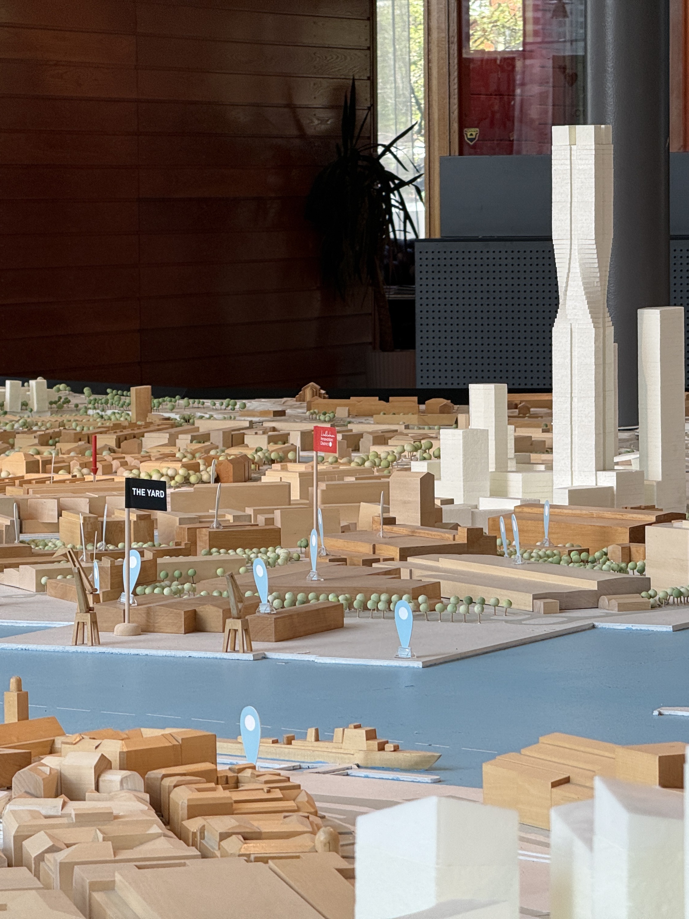 The Älvstaden city model in Gothenburg at 1:400. The existing city in wood, planned buildings in white, the river in light blue with harbour cranes, and small flags marking The Yard and Lindholmen Innovation District. Karlatornet rises at the centre.